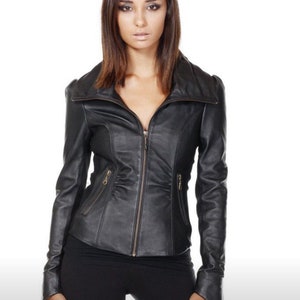 Puede incluir: Chaqueta de cuero negra con cremallera, cuello alzado y corte entallado. La chaqueta tiene dos peque&ntilde;os bolsillos con cremallera y se lleva con pantalones negros. El fondo es blanco.