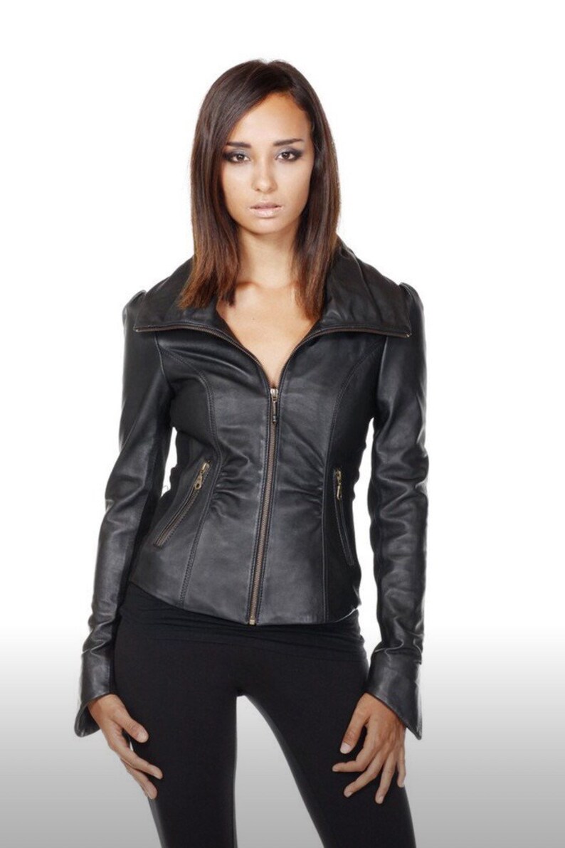 Puede incluir: Chaqueta de cuero negra con cremallera, cuello alzado y corte entallado. La chaqueta tiene dos peque&ntilde;os bolsillos con cremallera y se lleva con pantalones negros. El fondo es blanco.