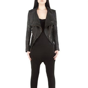 Puede incluir: Chaqueta de cuero negra con cuello asim&eacute;trico y detalles de cremallera. La chaqueta se combina con una camiseta negra y pantalones negros. Los pantalones tienen un dise&ntilde;o de tiro bajo &uacute;nico. El modelo est&aacute; sobre un fondo blanco.