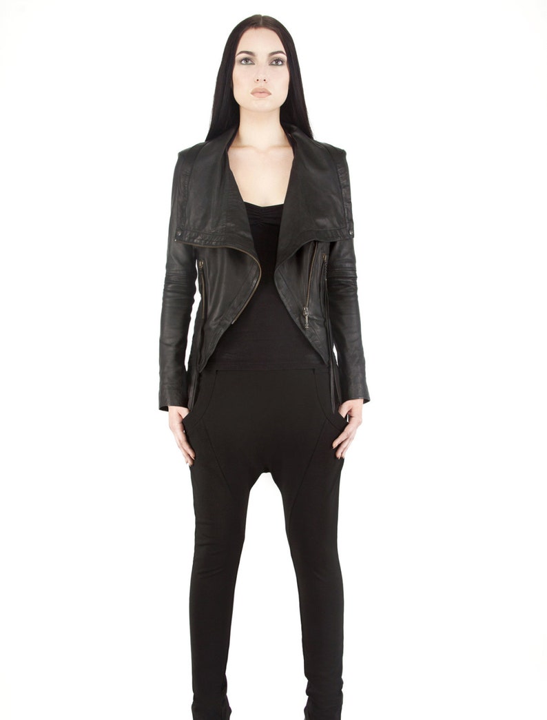 Puede incluir: Chaqueta de cuero negra con cuello asim&eacute;trico y detalles de cremallera. La chaqueta se combina con una camiseta negra y pantalones negros. Los pantalones tienen un dise&ntilde;o de tiro bajo &uacute;nico. El modelo est&aacute; sobre un fondo blanco.
