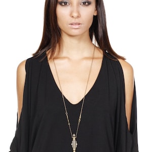 May include: A gold chain necklace with a decorative pendant shaped like a small, ornate bottle. The bottle is clear and has a black and white striped design.