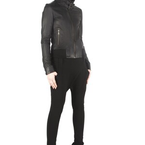 May include: A black leather jacket with a hood and a zipper closure. The jacket has a fitted silhouette and a cropped length. The model is wearing black pants and black heeled shoes.