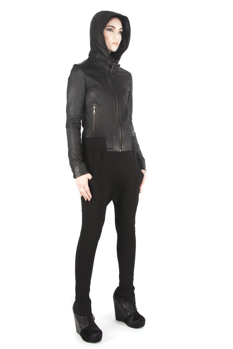 May include: A black leather jacket with a hood and a zipper closure. The jacket has a fitted silhouette and a cropped length. The model is wearing black pants and black heeled shoes.