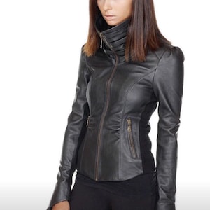 May include: Black leather jacket with a high collar and a zipper closure. The jacket has long sleeves and a fitted silhouette. The model is wearing black pants. The background is white.