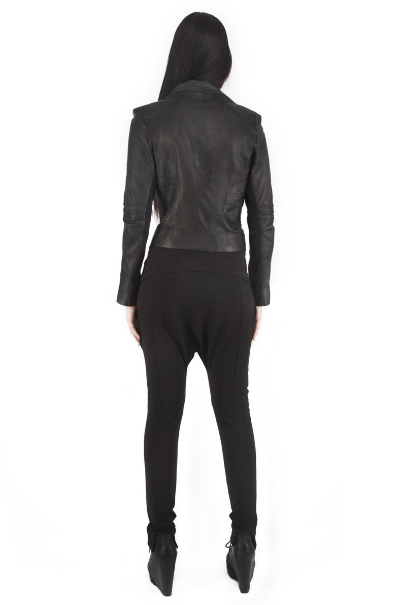 Puede incluir: Chaqueta de cuero negra con detalles en los hombros y un conjunto negro a juego. La chaqueta tiene un corte entallado y los pantalones tienen una silueta holgada &uacute;nica. El conjunto se completa con botines negros con cu&ntilde;a.