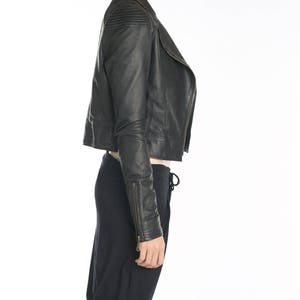 May include: A black leather jacket with a zipper closure and a cropped length. The jacket has a stand-up collar and a zippered pocket on the left sleeve.