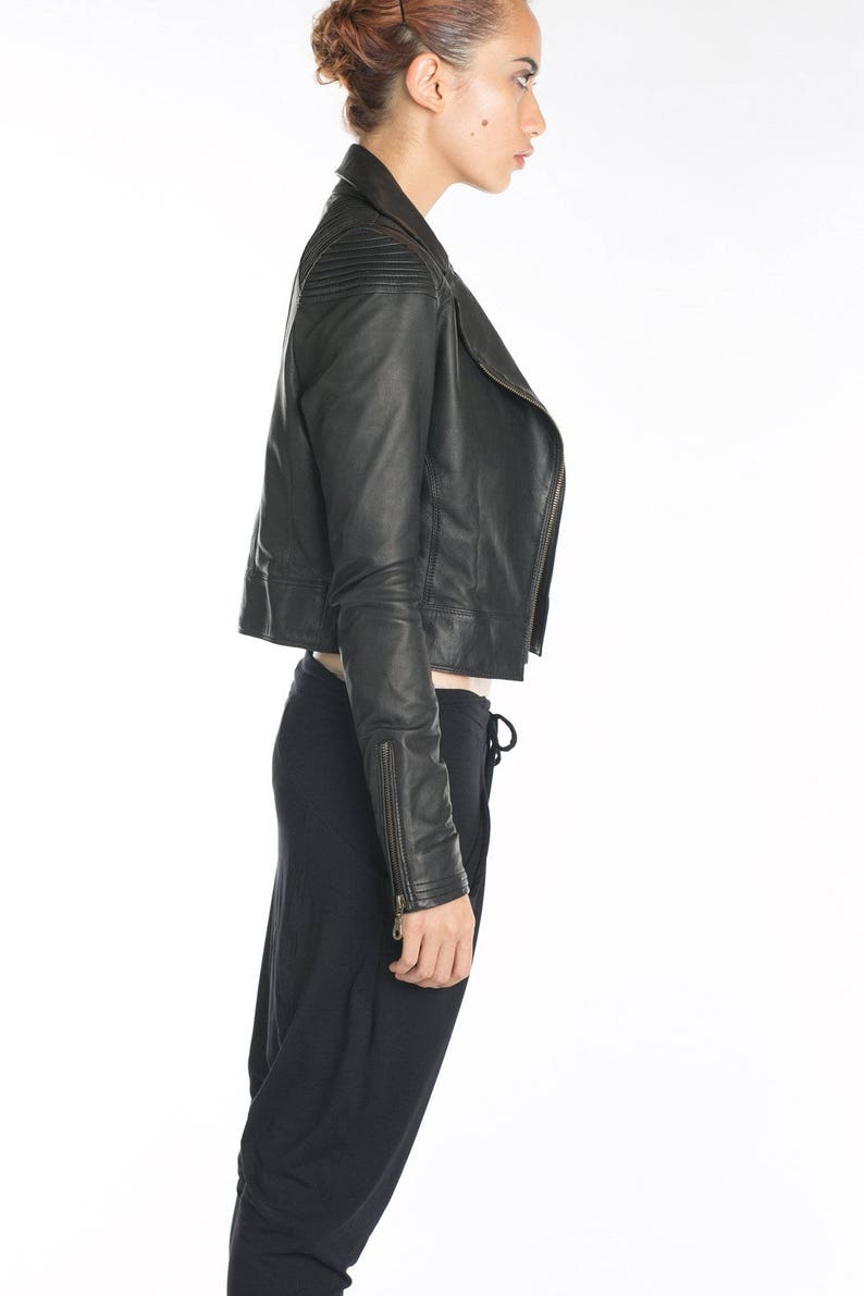 May include: A black leather jacket with a zipper closure and a cropped length. The jacket has a stand-up collar and a zippered pocket on the left sleeve.