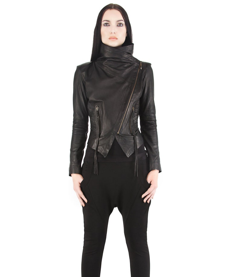 Puede incluir: Chaqueta de cuero negro con cremallera asim&eacute;trica y cuello alto. La chaqueta tiene mangas largas y m&uacute;ltiples bolsillos con cremallera. El modelo lleva pantalones negros. Una prenda de vestir elegante.