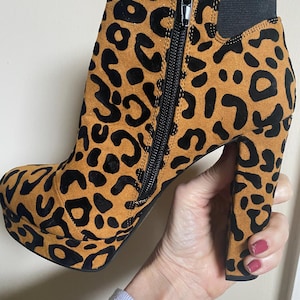 May include: Brown suede ankle boots with a black leopard print and a chunky black heel. The boots have a side zipper and a platform sole.