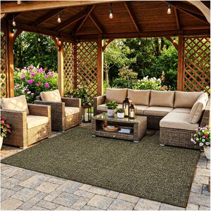 May include: Outdoor patio set with a brown woven sofa, two armchairs, and a coffee table, all with beige cushions. A large green rug covers the patio floor. The setting is under a wooden gazebo with string lights, surrounded by greenery.