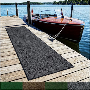 May include: A long, rectangular, dark gray outdoor carpet with a black border is laid out on a wooden dock. A classic wooden boat is docked nearby on a lake. The carpet is likely used for boats, patios, or entryways.
