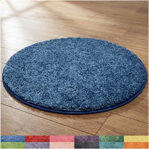 May include: A circular blue rug with a thick, shaggy pile texture and a matching blue fabric border. The bottom of the image displays a color palette strip showing the rug available in twelve different solid colors including red, green, and yellow.