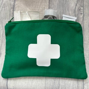 May include: A green first aid kit with a white cross emblem. The zipped pouch contains medical supplies, including a bottle and cotton buds. The kit is designed for emergency medical situations and first aid.