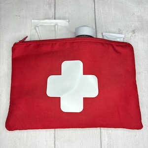 May include: Red canvas zippered pouch with a white cross on the front. The pouch is filled with various items, including cotton buds, a small bottle, and a tube of cream.