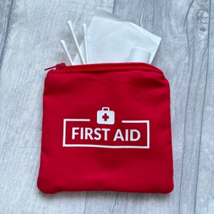 May include: A red zipped pouch with the words "FIRST AID" in white, and a white medical cross symbol. The pouch is open, showing white cotton buds, tissues, and a small white container.