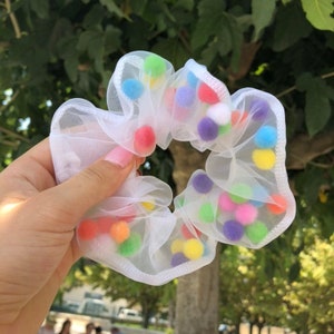 May include: White mesh hair scrunchie with colourful pom poms.
