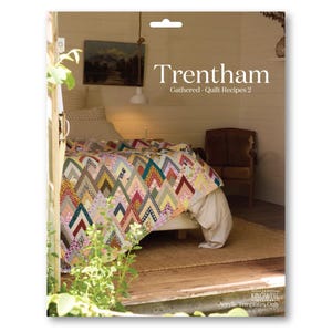 May include: A vibrant quilt with a chevron design adorns a bed in a snug room. The quilt incorporates diverse fabrics in hues of red, green, yellow, and blue. The book cover reads "Trentham, Gathered - Quilt Recipes 2".