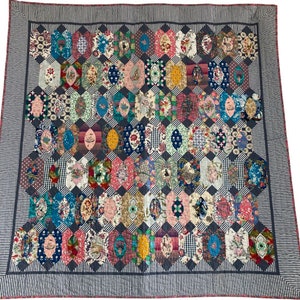 May include: A colorful quilt with a geometric pattern of hexagons and ovals. The quilt is made of various fabrics with floral and geometric prints. The quilt is bordered with a black and white striped fabric.