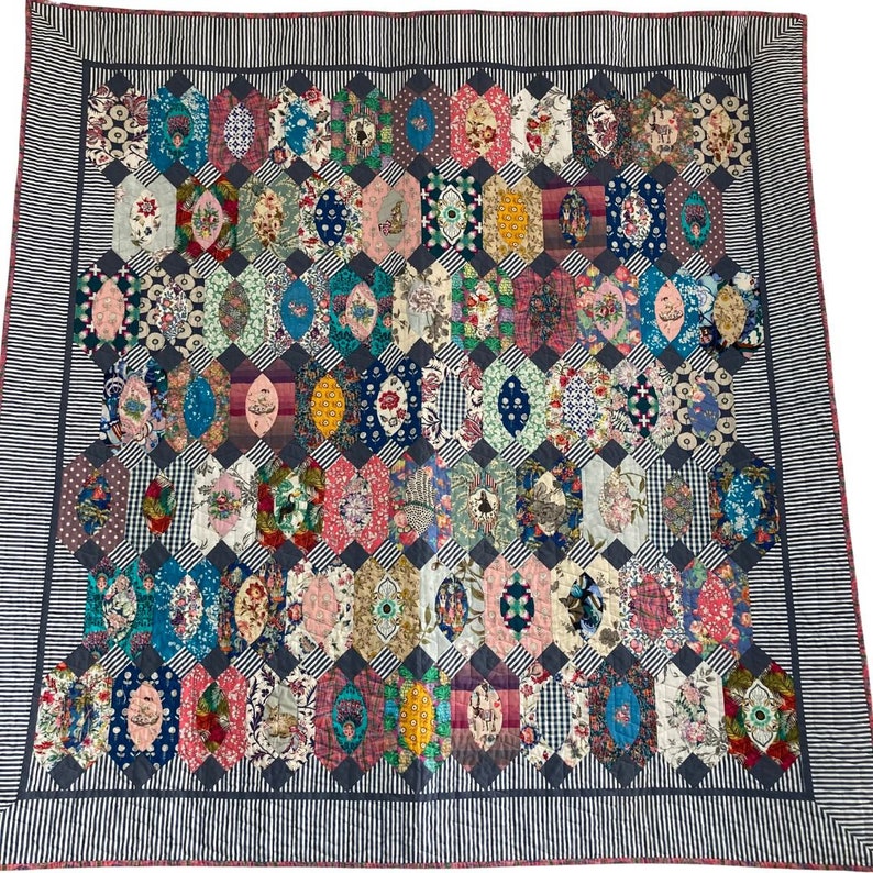 May include: A colorful quilt with a geometric pattern of hexagons and ovals. The quilt is made of various fabrics with floral and geometric prints. The quilt is bordered with a black and white striped fabric.