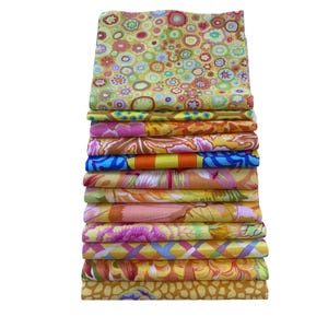 May include: A pile of patterned fabric squares in a variety of colours. The fabrics display floral and geometric designs in shades of yellow, orange, pink, blue, and green. The patterns include flowers, circles, and abstract designs, creating a vibrant display.
