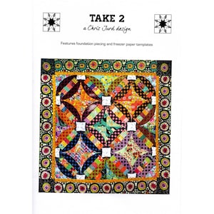 May include: A vibrant quilt pattern with the text "TAKE 2 a Chris Jurd design". The quilt showcases a central design of intersecting circles and squares in various colours and patterns, framed by a decorative border.