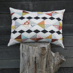 May include: A patchwork cushion with a geometric design in shades of red, orange, yellow, blue, and black. The cushion is sitting on a tree stump. The text "CLOPIN BY JEN KINGWELL" is at the bottom of the image. The text "ACRYLIC TEMPLATES ONLY Pattern featured in Quilt Recipes Book" is at the bottom of the image.