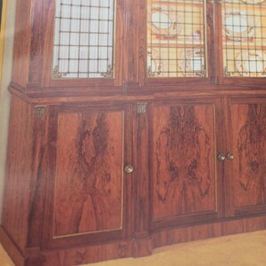 May include: A wooden cabinet with glass doors and drawers. The cabinet has a dark wood finish and brass accents. The glass doors are decorated with a grid pattern.