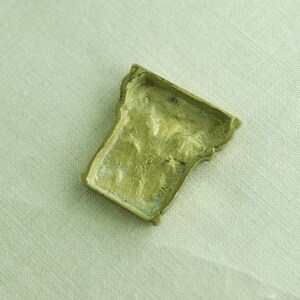 May include: A small, ornate, brass-colored metal object with a detailed design. The object is shaped like a small, upside-down cup.