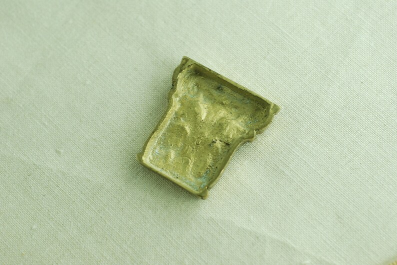 May include: A small, ornate, brass-colored metal object with a detailed design. The object is shaped like a small, upside-down cup.