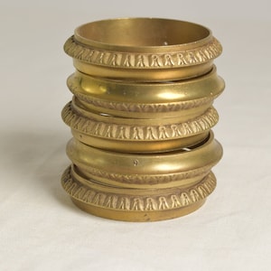 Puede incluir: Un conjunto de cinco anillos de servilleta de metal dorado con bordes decorativos.