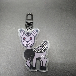May include: A black and white cartoon deer keychain with red eyes and a black and white polka dot pattern. The keychain is made of clear acrylic and has a black metal zipper pull.