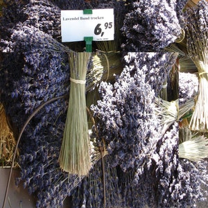 May include: A bunch of dried lavender flowers tied together with twine. The lavender is a light purple colour and the twine is a natural brown colour. The price tag reads "Lavende Bund trocken 6,95".