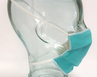 May include: A turquoise blue face mask with white elastic ear loops. The mask is made of a soft, breathable fabric and has a pleated design.
