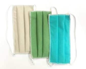 May include: Three fabric face masks with white elastic straps. The masks are beige, green, and turquoise.