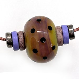 May include: A yellow and brown glass bead with black polka dots, strung on a copper wire with purple and silver spacer beads.