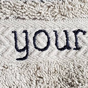 May include: A light gray towel with the embroidered text "wash your paws" in navy blue. The text is centered on a textured band with a chevron pattern.