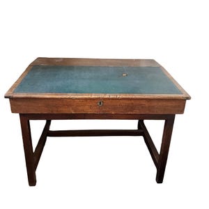 May include: An antique wooden desk with a dark green leather writing surface. The desk has a rectangular shape with a drawer and a keyhole. The legs are angled and connected by a stretcher. The wood has a warm, brown tone.