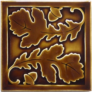May include: A square ceramic tile with a glossy dark brown finish featuring a raised relief design of two oak leaves and two acorns. The leaves and acorns are outlined in a lighter brown tone, creating a distinct contrast against the darker background.