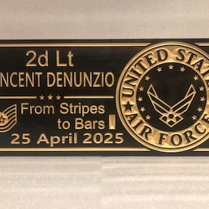 May include: A black plaque with gold lettering and a gold United States Air Force emblem. The plaque reads "2d Lt Vincent Denunzio From Stripes to Bars 25 April 2025".