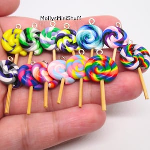 May include: A collection of miniature lollipop charms featuring various swirl patterns in bright colors including yellow, green, purple, blue, pink, and rainbow. Each charm has a small silver metal loop at the top and a thin tan stick at the base.