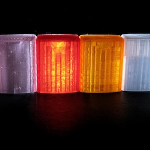May include: Four cylindrical objects in a row, each with a different color. From left to right, they are pink, red, orange, and blue. The objects have a ribbed texture and are lit from within, creating a glowing effect.