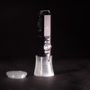 May include: A black flashlight with a silver button and a clear plastic base. The flashlight is sitting on a black surface.