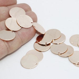 Peut inclure: Plusieurs disques métalliques ronds et plats de couleur or rose, avec un petit trou près du bord. Les disques sont dispersés, certains sont tenus dans une main, d'autres reposent sur une surface blanche. Ce sont probablement des composants de bijoux.