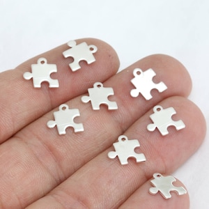 May include: A collection of small, silver-colored puzzle piece charms. Each charm has a loop at the top for attaching to jewelry or other crafts. The charms are displayed against a light background.