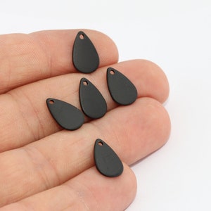 May include: A collection of six matte black teardrop-shaped charms. Each charm has a small hole at the top for stringing. The charms are displayed against a white background.