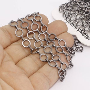 May include: Close-up of a gunmetal-colored chain with circular links. The chain is held in a hand, with a portion of the chain coiled in the background. The tag reads "jk jewelryMetal".
