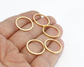 May include: A hand holds several gold-colored oval-shaped jewelry findings. The findings are thin and have a smooth, polished surface. The background is plain white, highlighting the jewelry components.