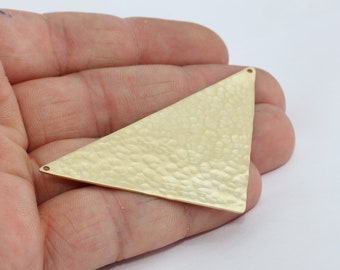 Peut inclure: Un composant de bijouterie triangulaire doré, à texture martelée, avec deux petits trous pour la fixation. La pièce métallique est tenue dans une main sur fond blanc. Idéal pour la création de bijoux.