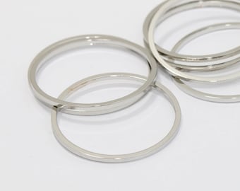 May include: Several silver-colored bangles are arranged on a white surface. The bangles are circular and appear to be made of metal. The image is well-lit, highlighting the smooth, reflective surfaces of the jewelry.