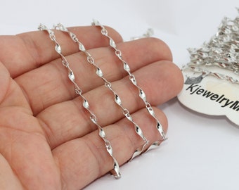 May include: A length of silver chain with a twisted, wavy design. The chain is held in a hand, with a roll of the same chain visible. The tag reads "kjewelryMetal".